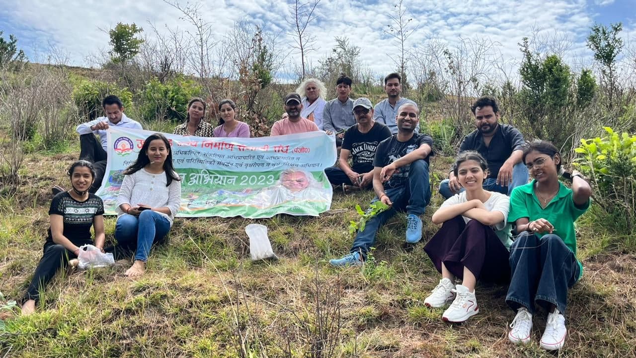 Volunteers of Vrikshabandhan Abhiyan 2023 seated on a grassy hillside with the campaign banner, Manoj Dhyani among them